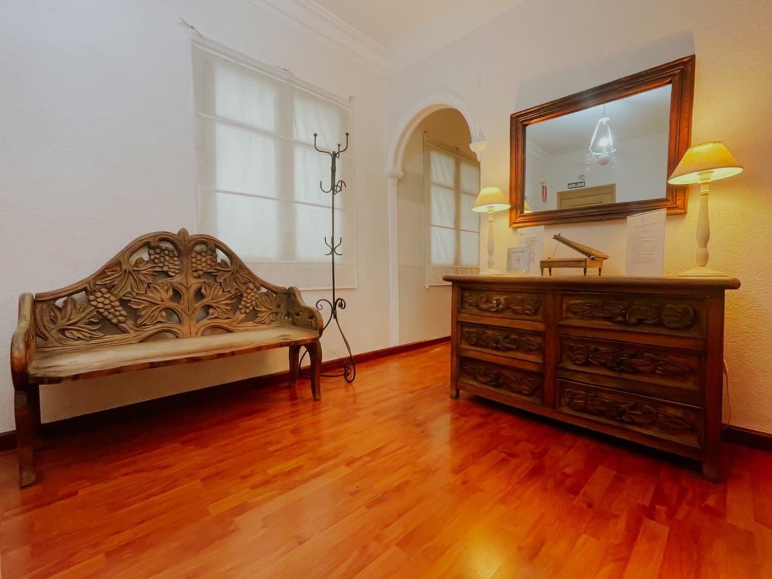 Sala de espera de Psyteco: un banco de madera tallada, un perchero de forja y una cómoda antigua con espejo, sobre suelo de tarima.