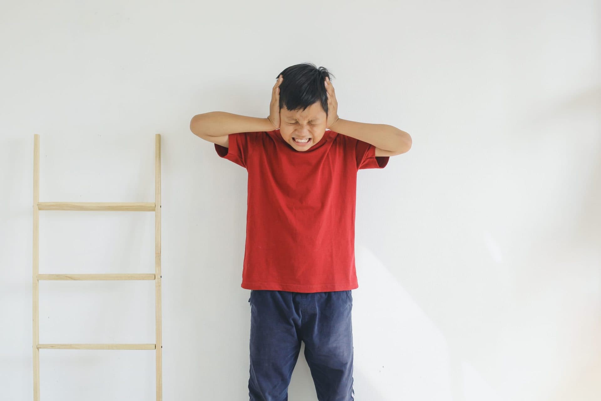 Niño con camiseta roja tapándose los oídos y apretando los ojos cerrados